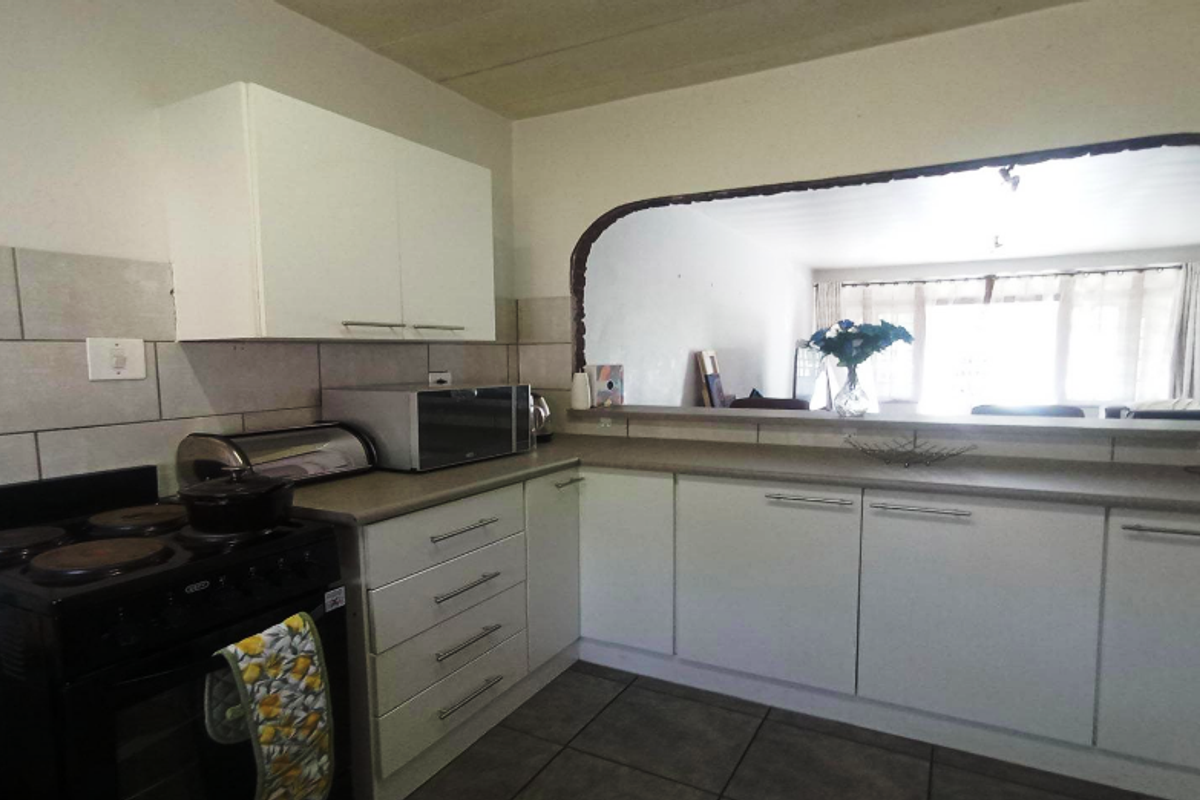 A functional kitchen featuring white cabinetry, tiled splashbacks, and a black freestanding stove, with a convenient serving hatch opening into the adjacent living area.