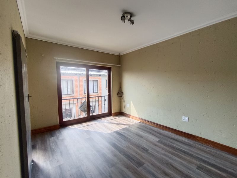 An empty bedroom featuring laminate flooring, a sliding glass door leading to a small balcony, and neutral wall finishes.
