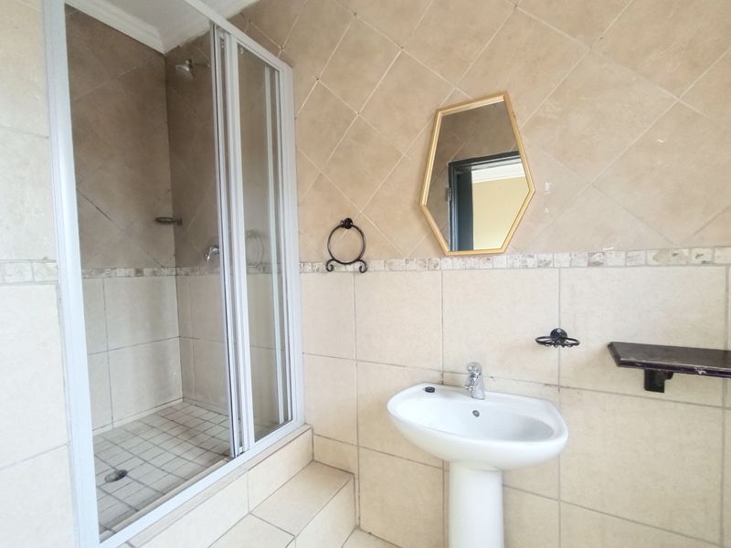 A functional bathroom featuring a pedestal basin, a tiled shower enclosure, and neutral wall tiling throughout.