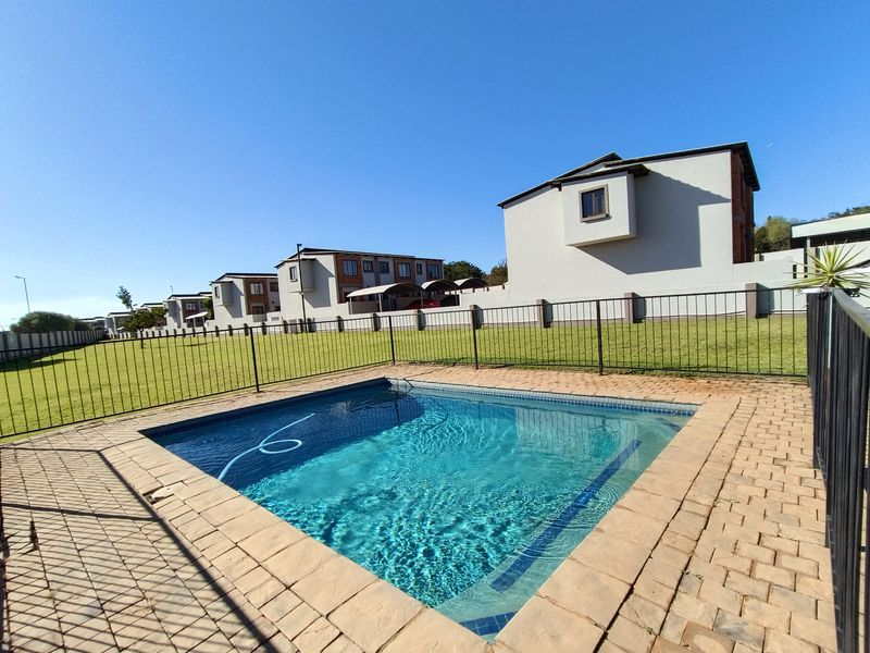 A well-maintained outdoor pool area featuring a clear swimming pool, paved surround, and secure metal perimeter fencing set within a spacious lawn.