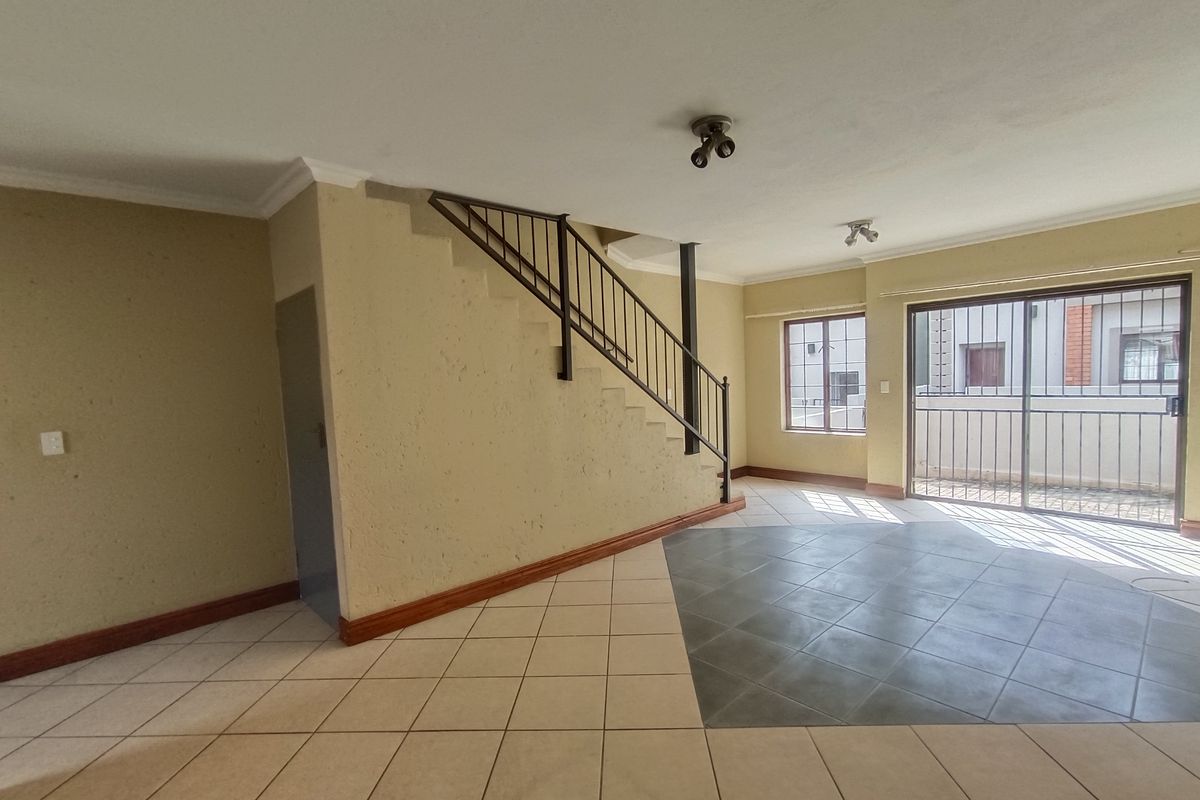 Spacious open-plan living area featuring a staircase with metal balustrade, tiled flooring, and sliding glass doors leading to an outdoor space.
