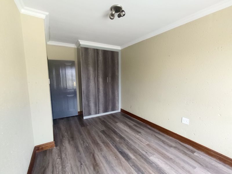 A clean, empty bedroom featuring modern laminate flooring, built-in cupboards, and neutral wall finishes, ready for personalization.