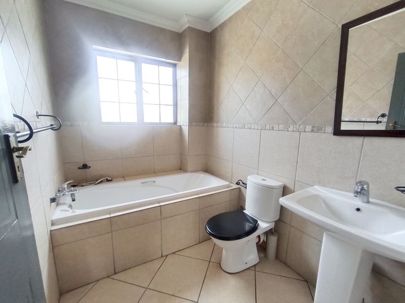 A functional bathroom featuring a built-in bathtub, pedestal sink, and toilet, finished with neutral wall and floor tiling.