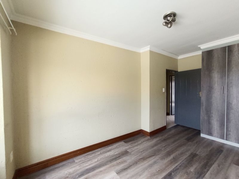 A bright, empty bedroom featuring modern laminate flooring, a built-in wardrobe, and neutral wall finishes, ready for personalization.