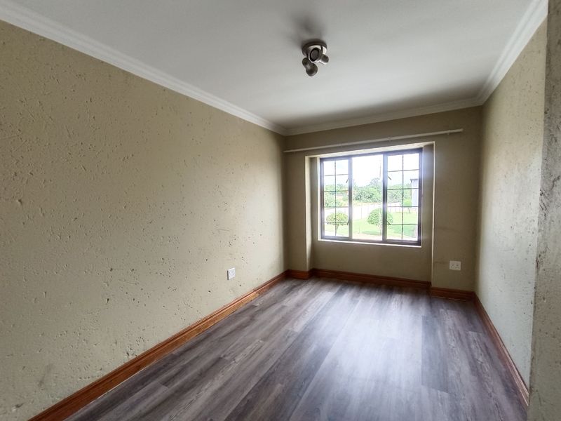 An empty bedroom featuring laminate flooring, textured walls, and a window with security bars, offering a blank canvas for personalization.