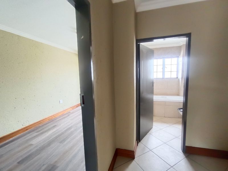 A view from a hallway looking into an empty bedroom and a bathroom featuring a built-in bathtub and tiled flooring.