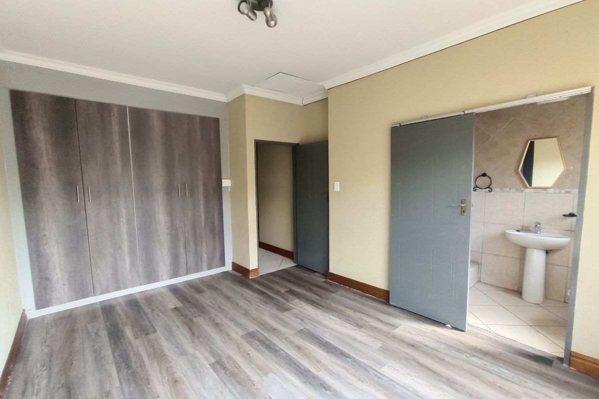 A vacant bedroom featuring laminate flooring, built-in cupboards, and an attached en-suite bathroom with a pedestal basin.