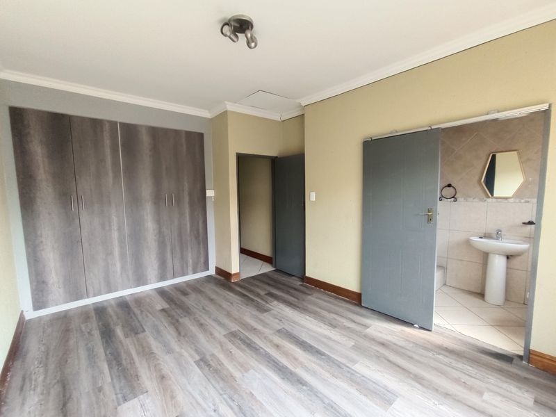 A vacant bedroom featuring laminate flooring, built-in cupboards, and an attached en-suite bathroom with a pedestal basin.