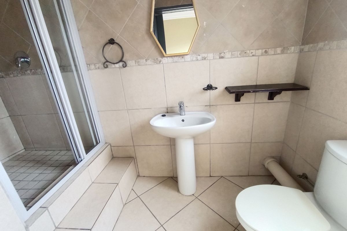 A functional bathroom featuring a pedestal basin, shower enclosure, and toilet, finished with neutral ceramic wall and floor tiles.