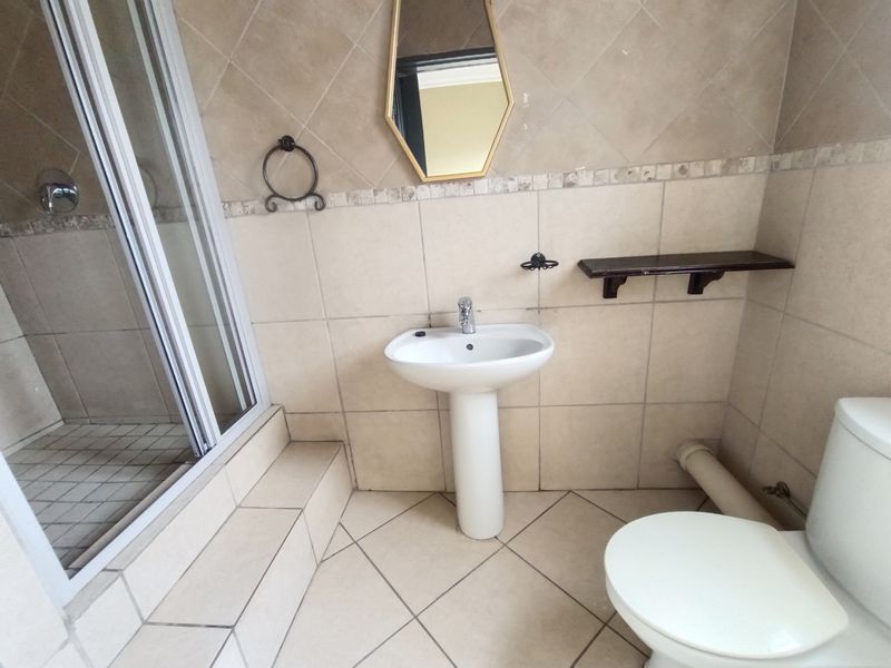 A functional bathroom featuring a pedestal basin, shower enclosure, and toilet, finished with neutral ceramic wall and floor tiles.