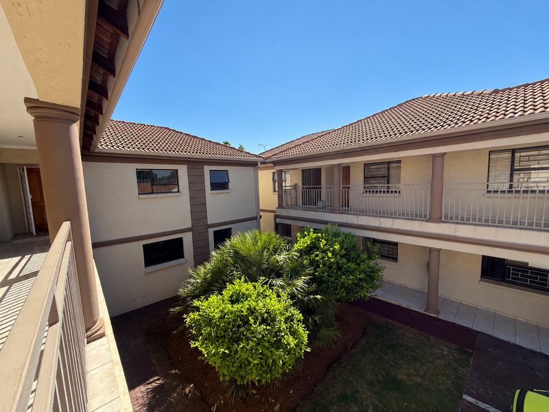 A view of the apartment complex courtyard featuring a central garden, paved walkways, and balconies with metal railings and concrete columns.