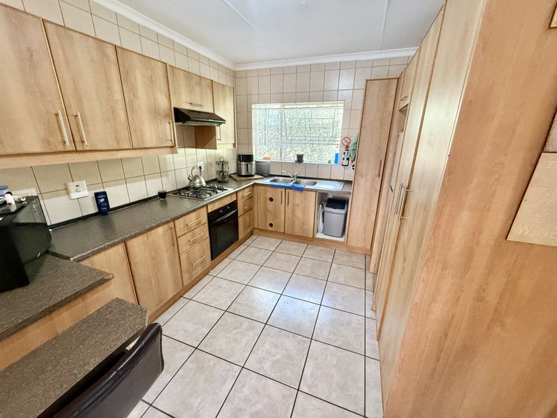 Functional kitchen featuring light wood-finish cabinetry, stone-look countertops, built-in oven, gas hob, and tiled flooring with ample storage space.