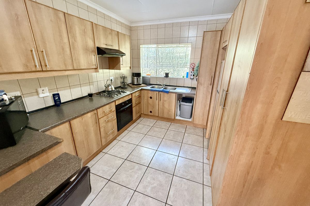 Functional kitchen featuring light wood-finish cabinetry, stone-look countertops, built-in oven, gas hob, and tiled flooring with ample storage space.