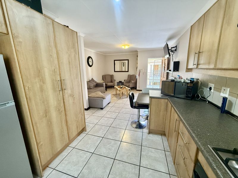 Open-plan living area featuring a functional kitchen with built-in cabinetry, laminate countertops, and tiled flooring, seamlessly flowing into the adjacent lounge space.