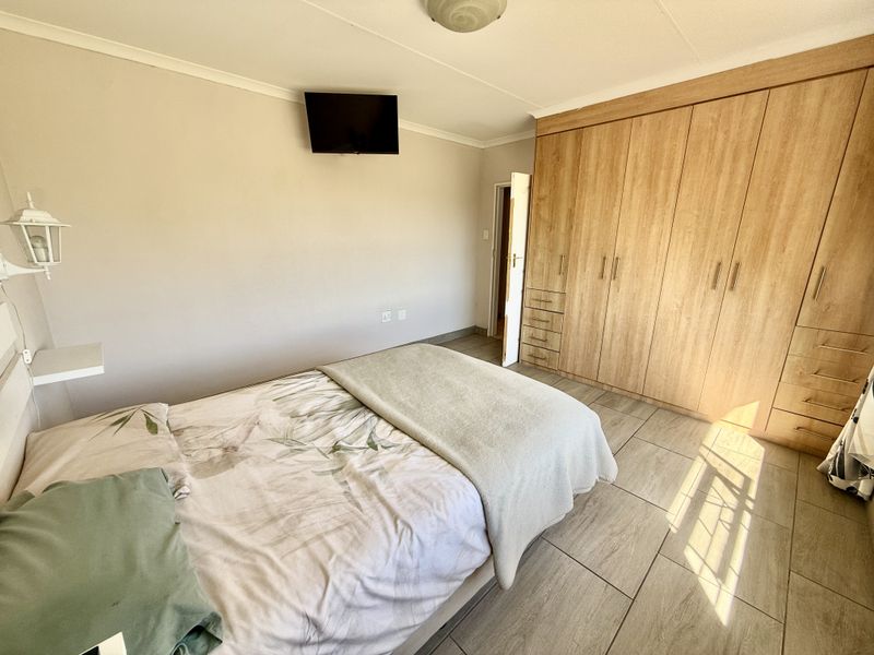 A well-maintained bedroom featuring extensive built-in wooden cupboards, neutral wall finishes, and durable tiled flooring.