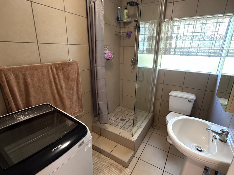 A functional bathroom featuring a pedestal basin, toilet, and a tiled shower enclosure with a glass screen and window for natural light.