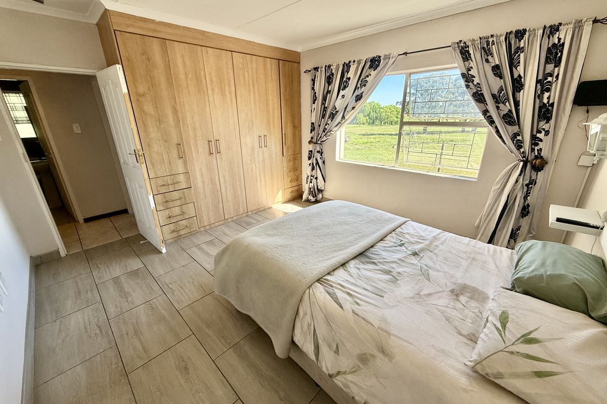 A well-lit bedroom featuring built-in wooden cupboards, tiled flooring, and a window offering a pleasant outdoor view.