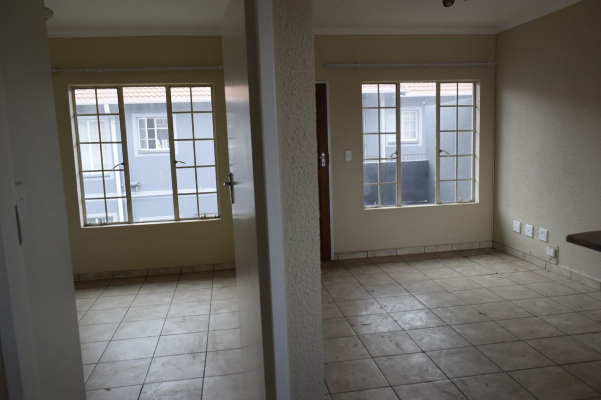 An empty, tiled living area featuring grid-pattern windows and neutral walls, offering a blank canvas for potential interior design updates.