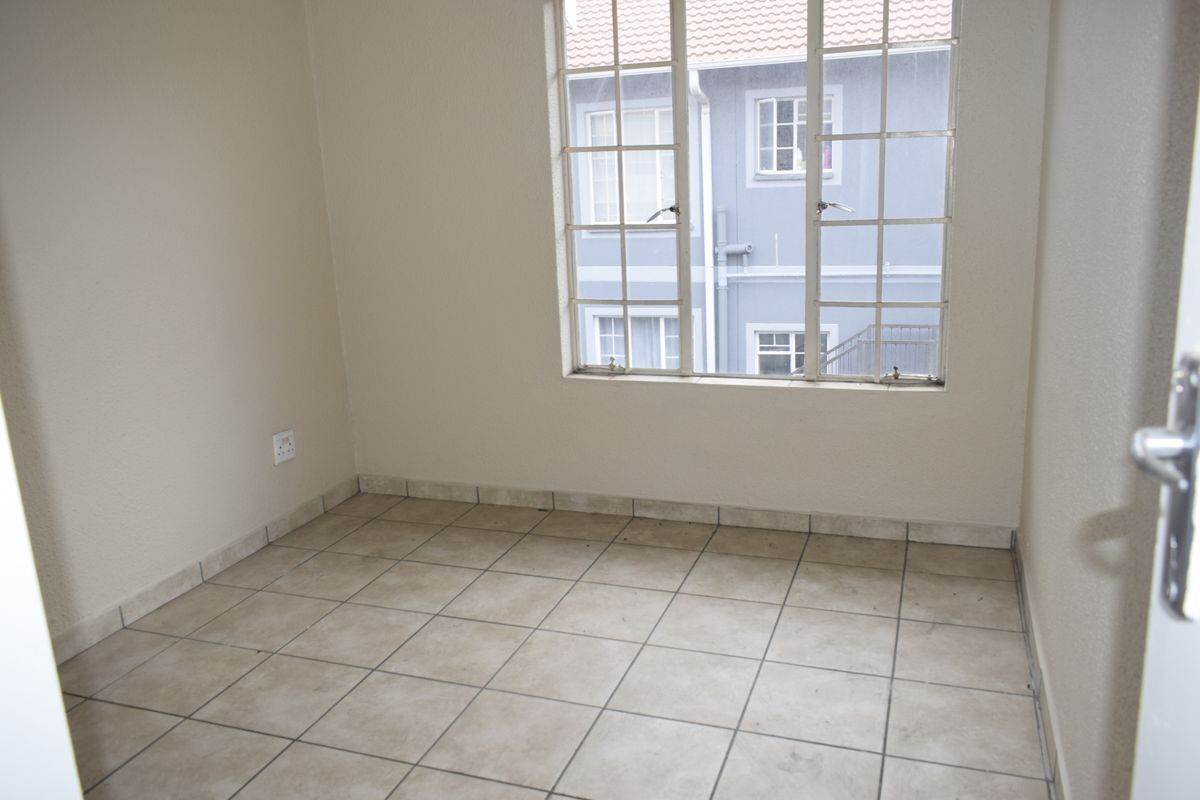 An empty bedroom featuring neutral tiled flooring and a large grid-pattern window, providing a blank canvas for personalization.