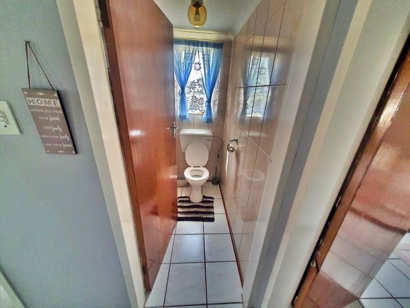A compact bathroom featuring a standard toilet, tiled walls, and tiled flooring, presenting a dated aesthetic suitable for modernization.