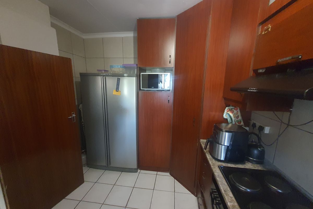 A functional kitchen featuring wood-finish cabinetry, tiled flooring, an integrated hob with extractor fan, and dedicated space for a large refrigerator.