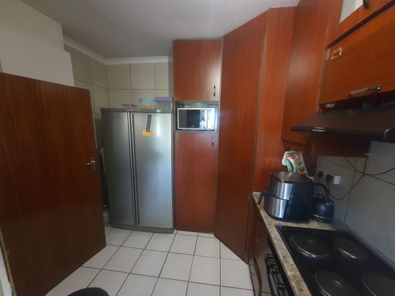 A functional kitchen featuring wood-finish cabinetry, tiled flooring, an integrated hob with extractor fan, and dedicated space for a large refrigerator.
