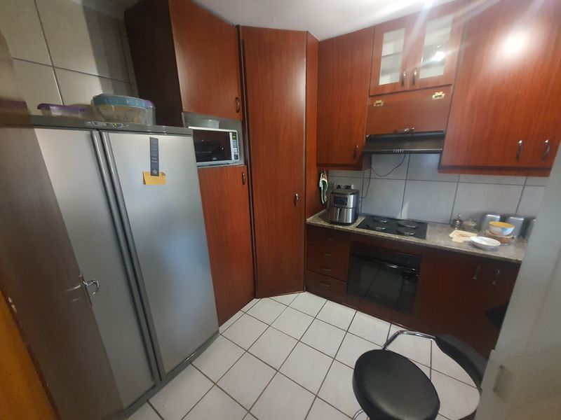 A functional kitchen featuring wood-finish cabinetry, tiled flooring, a built-in oven, and an electric hob with an extractor fan.
