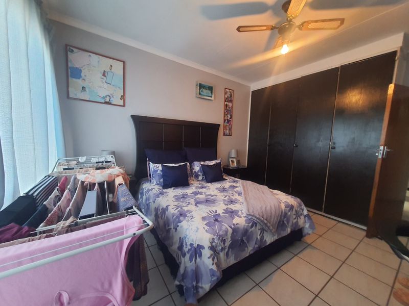 A bedroom featuring tiled flooring, a ceiling fan, and dark built-in cupboards providing ample storage space.