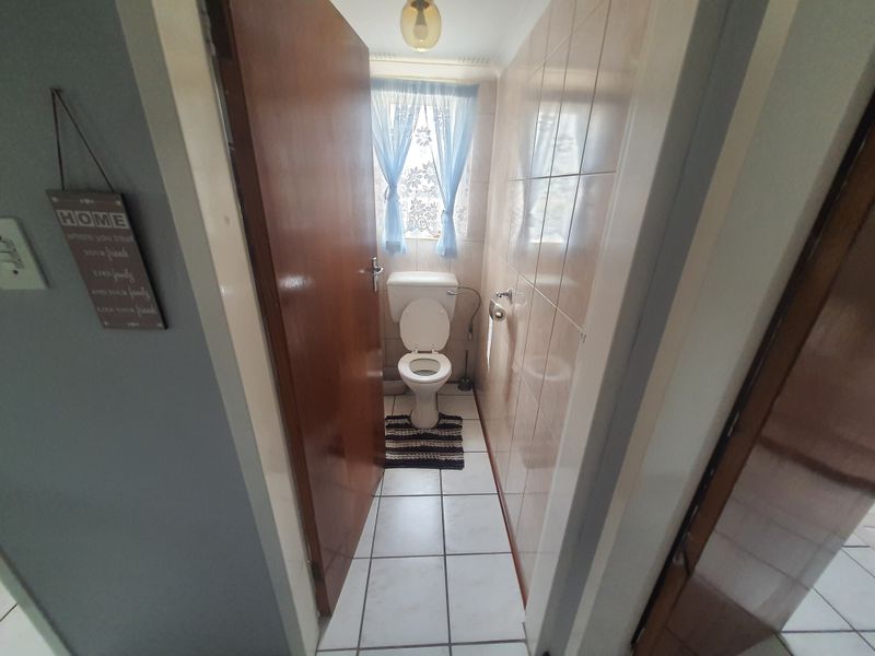 A compact bathroom featuring ceramic floor and wall tiles, equipped with a standard toilet and functional fixtures.