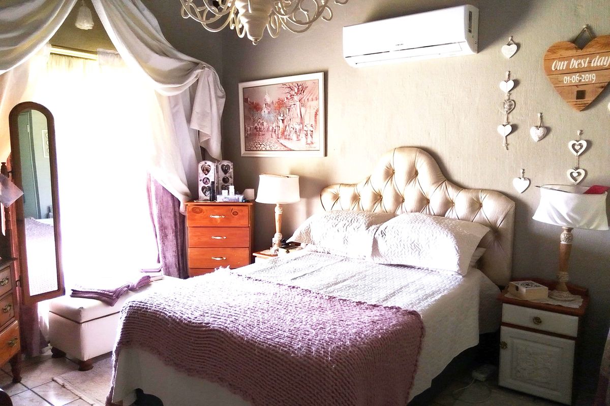 A cozy bedroom featuring a wall-mounted air conditioning unit, tiled flooring, and a large window with draped curtains.