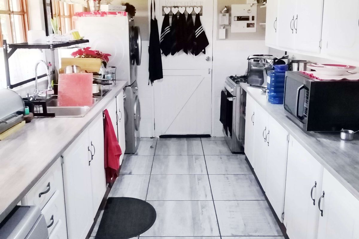 A functional galley-style kitchen featuring white cabinetry, laminate countertops, tiled flooring, and a vaulted ceiling with exposed beams.