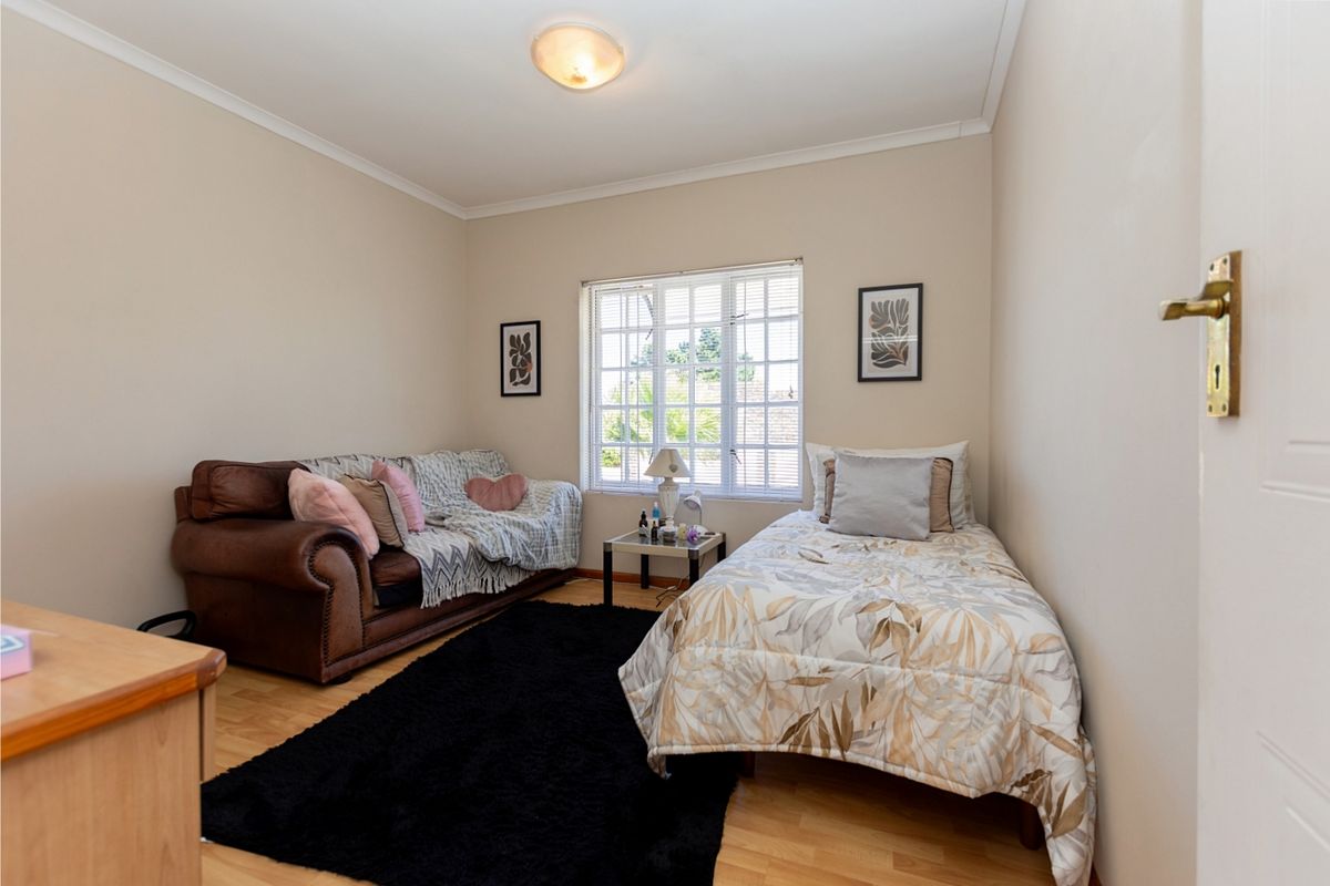 A functional bedroom featuring laminate flooring, neutral wall finishes, and a window fitted with security burglar bars.