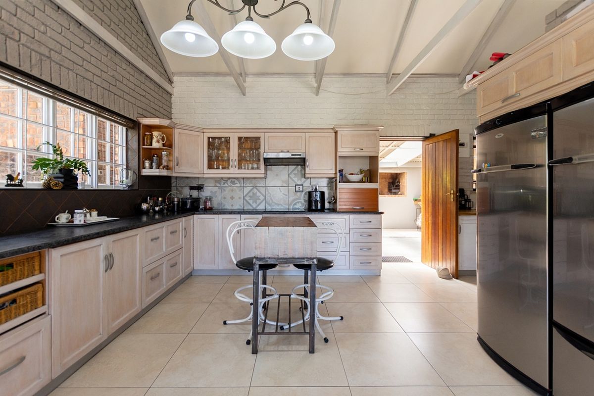 Spacious kitchen featuring light wood cabinetry, tiled splashbacks, exposed beam ceilings, and a brick feature wall, offering a bright and functional cooking space.