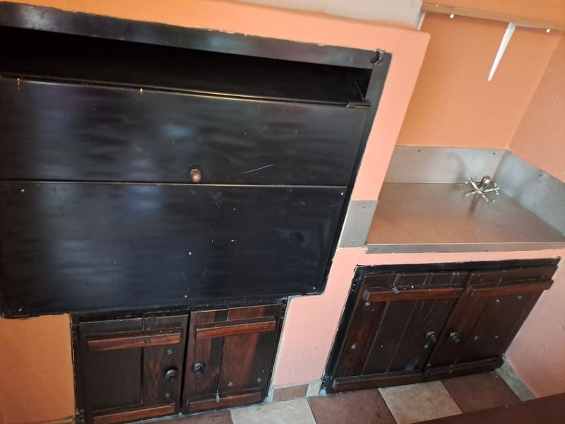 Outdoor entertainment area featuring a built-in braai, stainless steel prep counter with sink, and wooden storage cabinetry.
