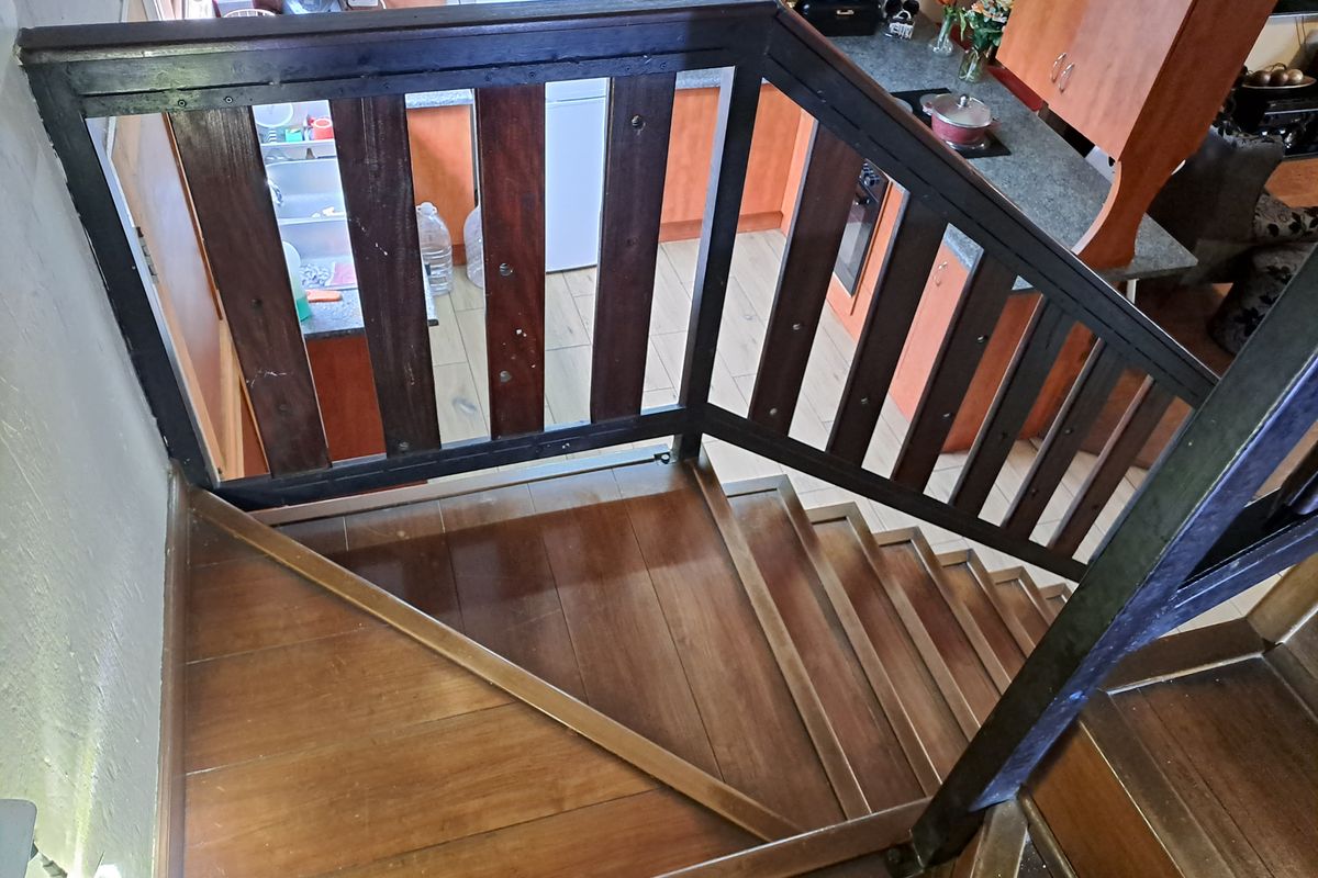 A view looking down a wooden staircase into a functional kitchen area featuring timber cabinetry, laminate countertops, and tiled flooring.