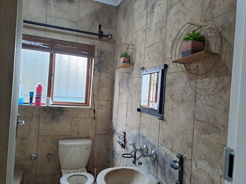 A compact bathroom featuring textured wall tiles, a wall-mounted basin, and a toilet, requiring cosmetic updates to improve the overall aesthetic.
