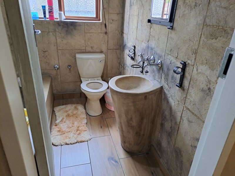 A compact bathroom featuring a unique pedestal basin, wall-mounted taps, and tiled finishes, requiring cosmetic updates to improve the overall aesthetic.