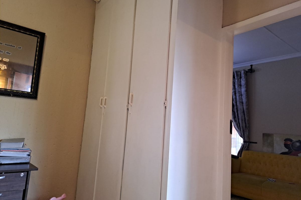 A bedroom interior featuring built-in cupboards and coving, with a view through the doorway into an adjacent living area.