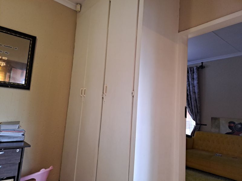 A bedroom interior featuring built-in cupboards and coving, with a view through the doorway into an adjacent living area.