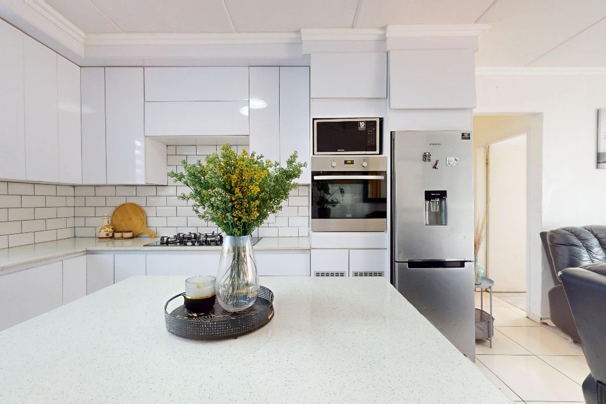 Modern kitchen featuring white gloss cabinetry, subway tile backsplash, stone countertops, a central island, and integrated stainless steel appliances.