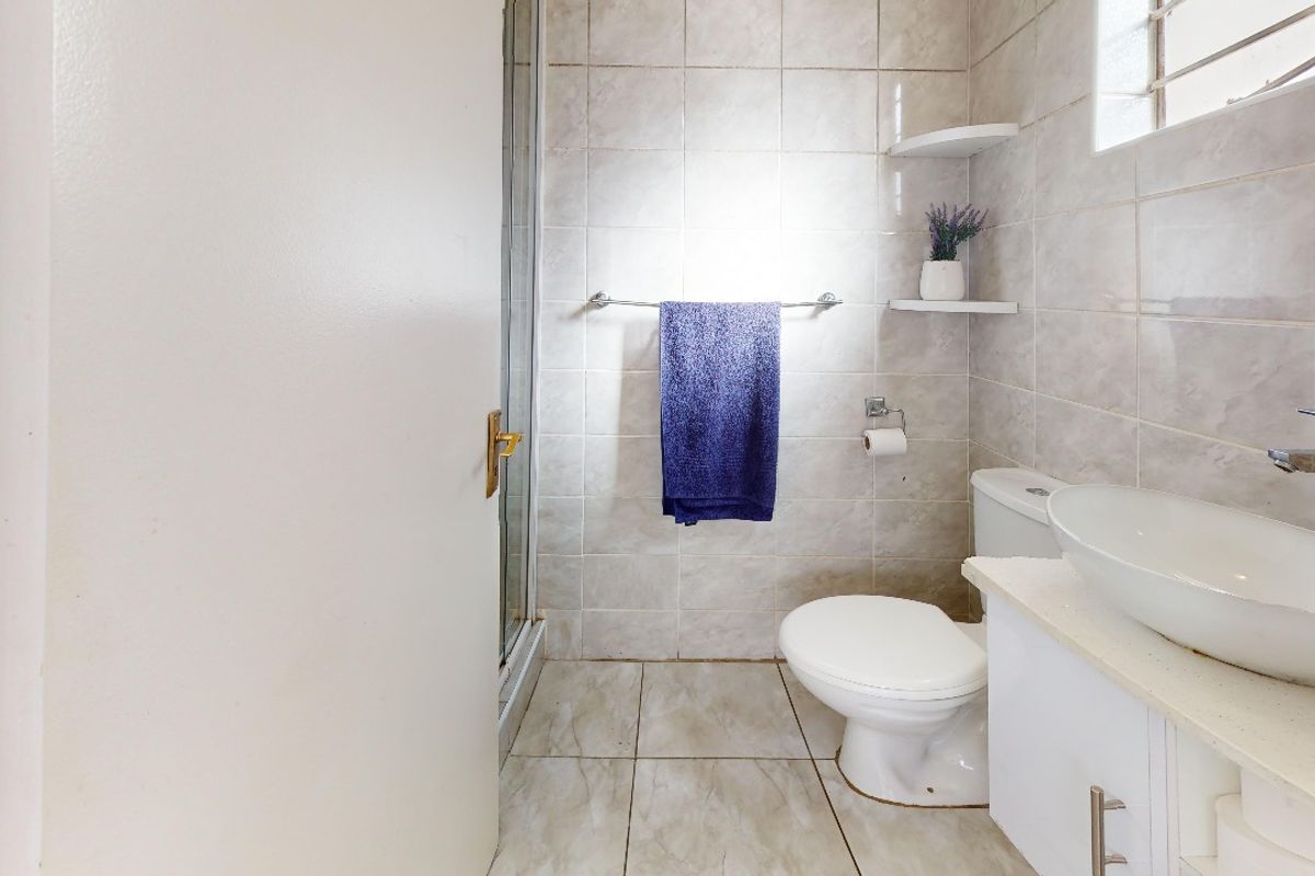 A functional bathroom featuring a shower enclosure, a modern vessel sink on a vanity cabinet, and neutral ceramic tiling throughout.