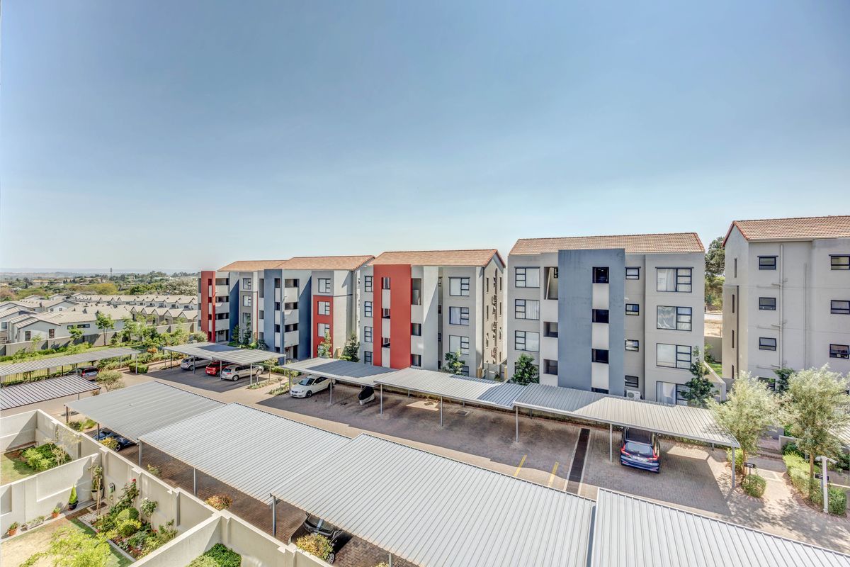 Aerial view of a modern apartment complex featuring multi-story residential buildings, covered parking structures, and paved communal areas.