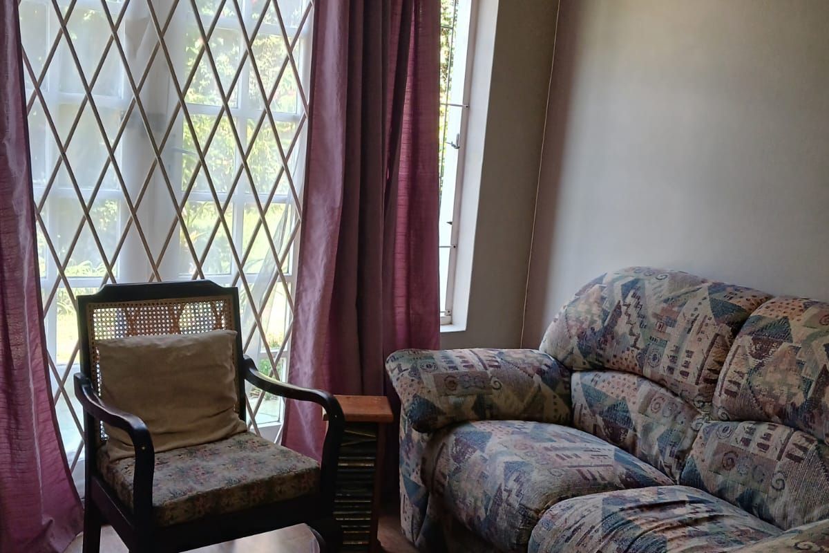 A living room area featuring laminate flooring and a large window fitted with a security gate.