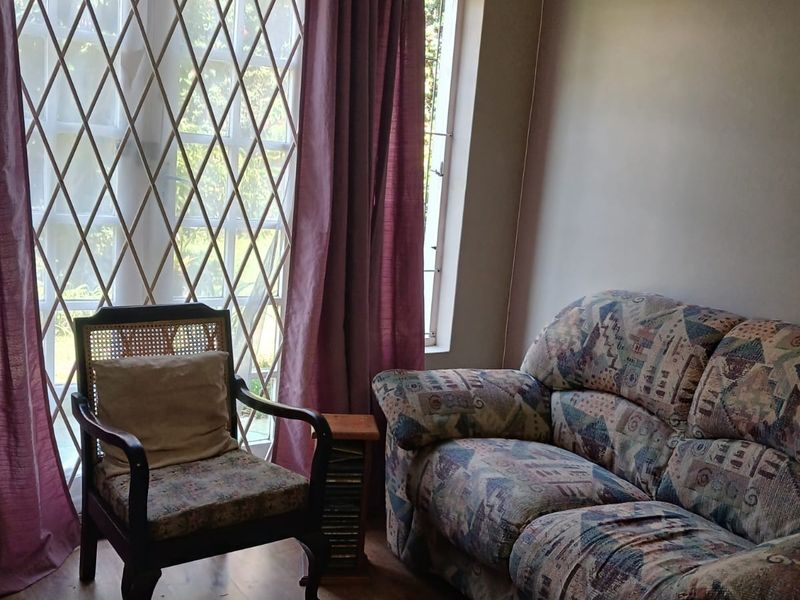 A living room area featuring laminate flooring and a large window fitted with a security gate.