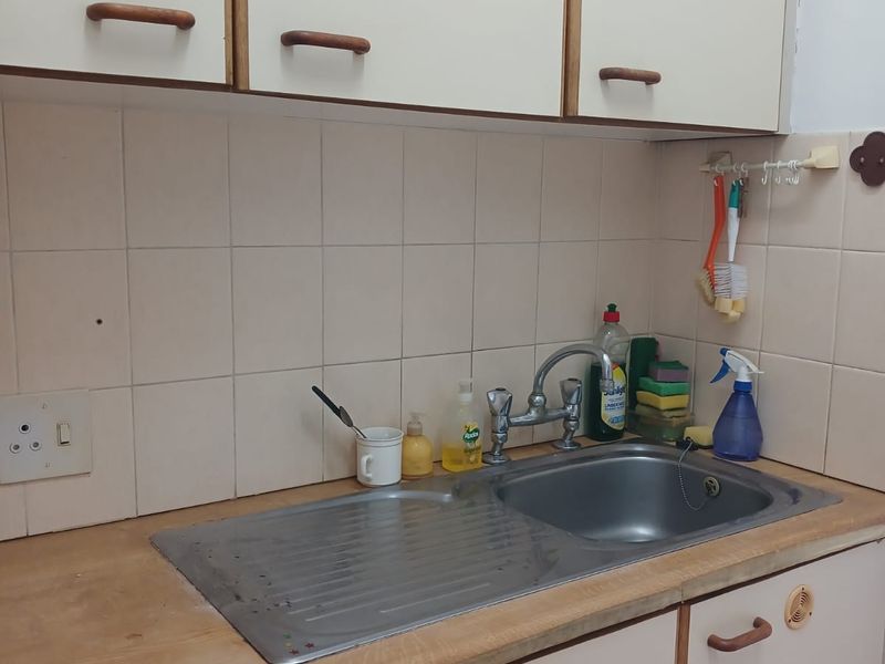 A dated kitchen sink area featuring laminate countertops, tiled backsplash, and original cabinetry, offering potential for a modern renovation.