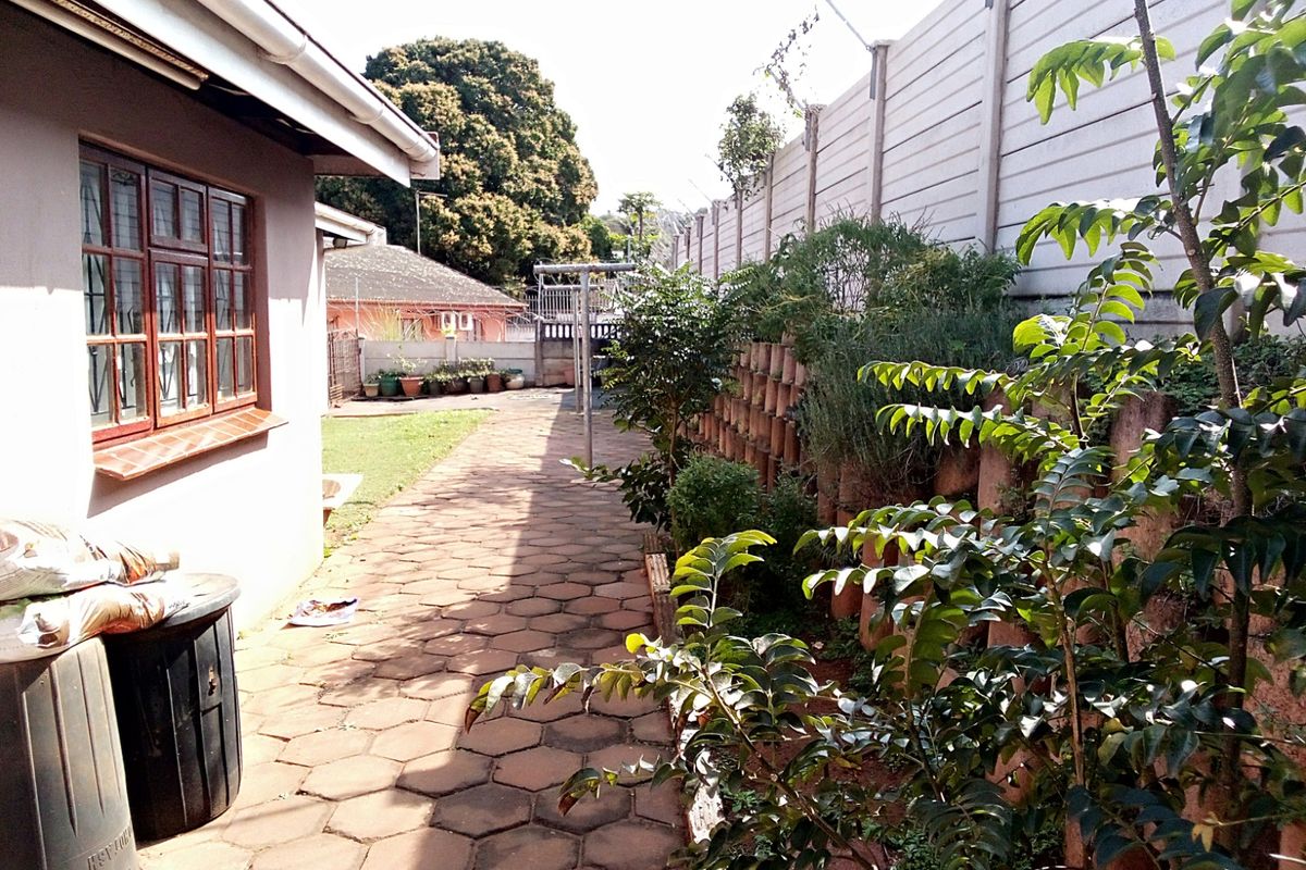 A side garden area featuring paved walkways, established greenery, and a high boundary wall, providing a functional outdoor space along the side of the house.