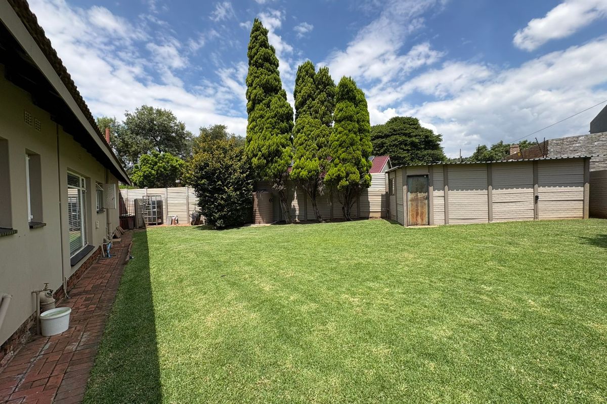 Spacious rear garden featuring a well-maintained lawn, brick paved walkway, and a detached storage shed enclosed by perimeter walling.
