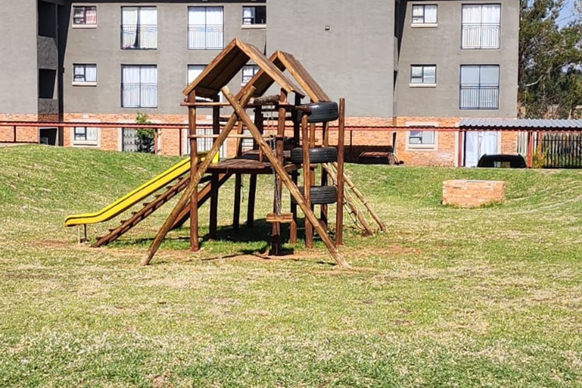 A view of the apartment complex rear exterior featuring a communal lawn area and playground equipment.