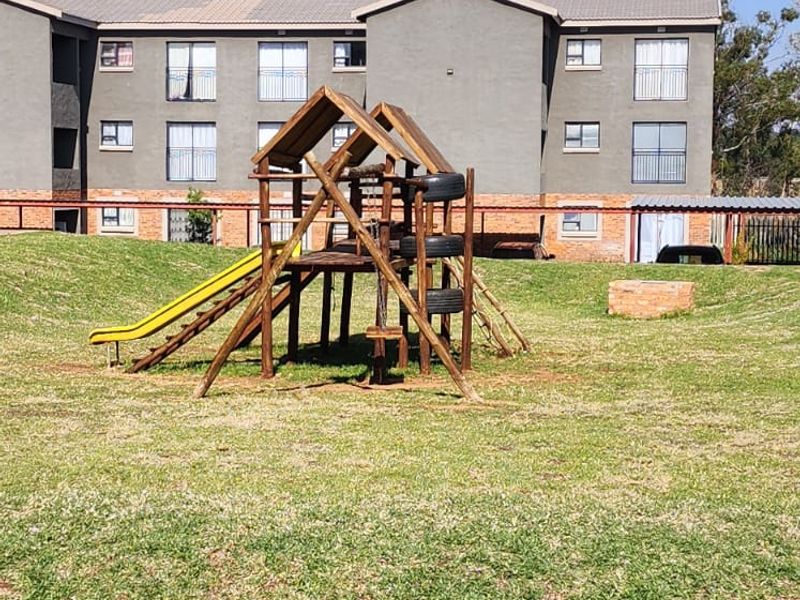 A view of the apartment complex rear exterior featuring a communal lawn area and playground equipment.