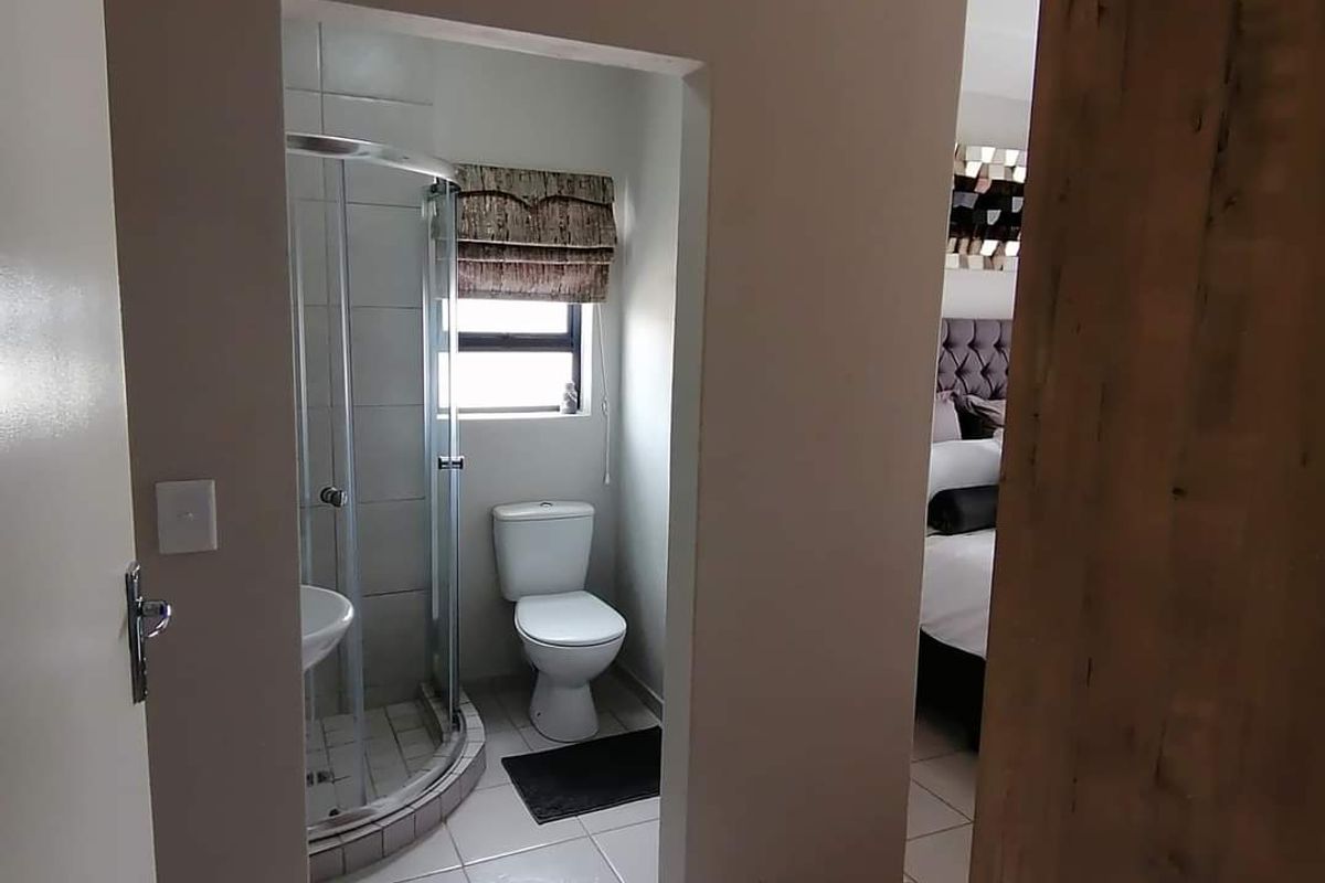 A functional en-suite bathroom featuring a corner shower enclosure, toilet, and tiled flooring, conveniently accessible from the adjacent bedroom.